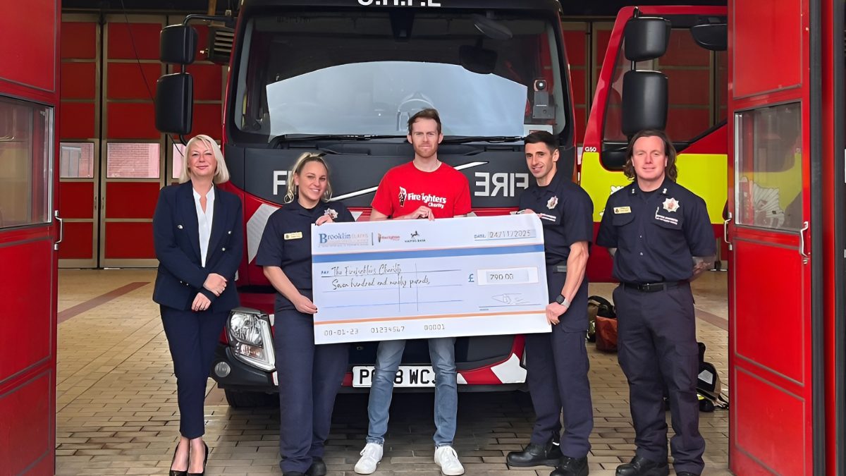 Brooklin Claims staff presenting a £790 charity cheque to firefighters at Bury Fire Station in front of a fire engine.