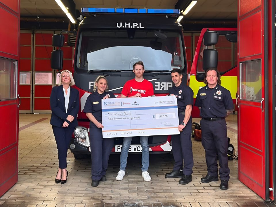 Brooklin Claims staff presenting a £790 charity cheque to firefighters at Bury Fire Station in front of a fire engine.